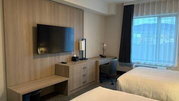 A hotel room with two beds, a desk with a chair, a television, and a window with curtains.