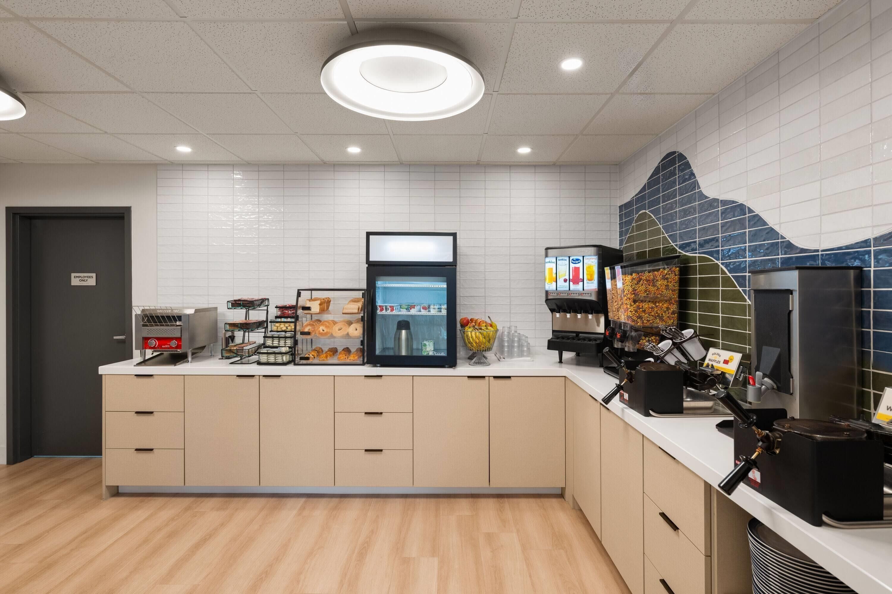 Un angolo colazione self-service con una macchina del caffè, un banco frigo e diverse opzioni alimentari.