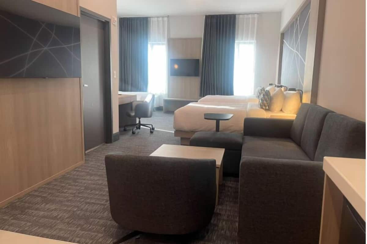 A hotel room with a sofa, a desk, a bed, and a TV.