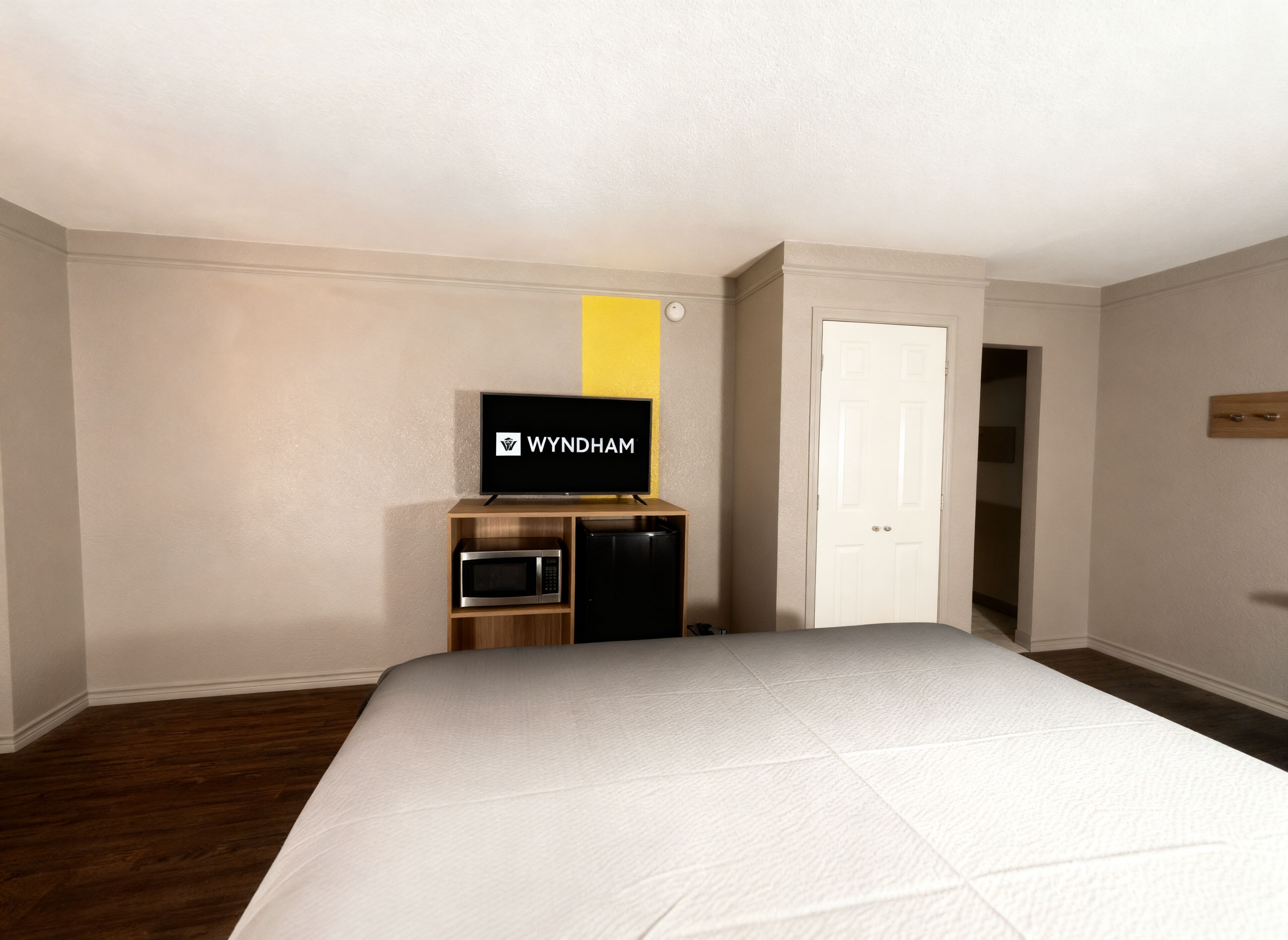 A hotel room with a bed, a television on a wooden stand, a microwave, and a door leading to another room.