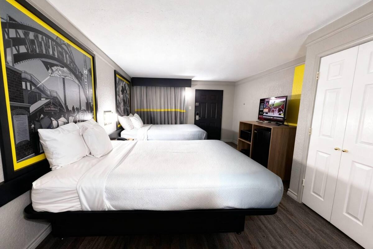 A hotel room with two beds, a television, a wardrobe, and a wall with a black and white mural.