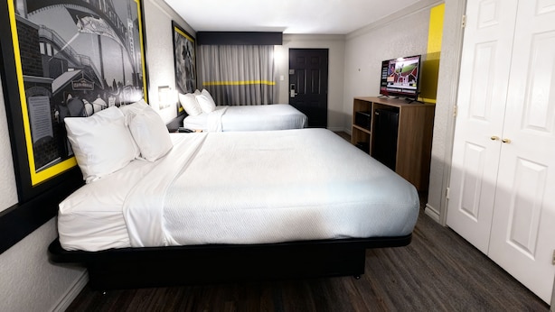 Une chambre d’hôtel avec deux lits, une télévision, un bureau et un grand tableau encadré au mur.