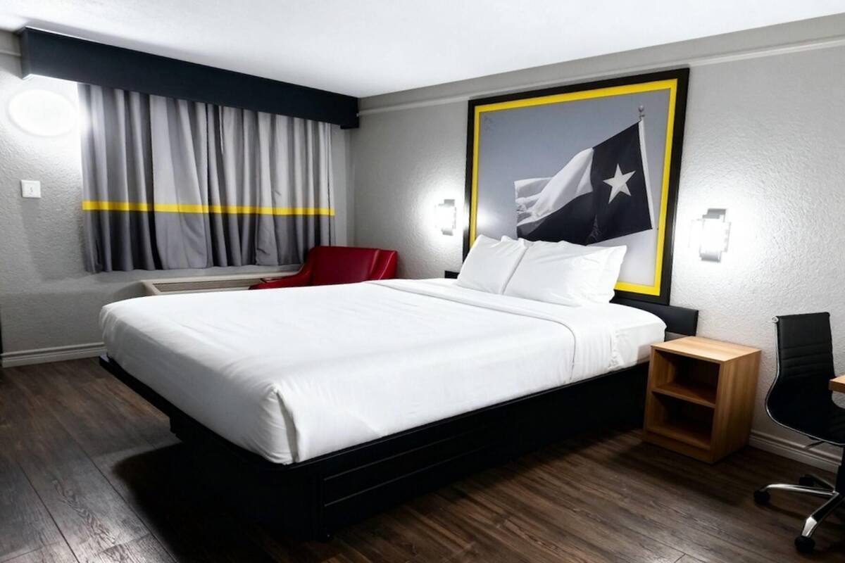 A hotel room with a large bed, a red chair, a desk, and a flag on the wall.