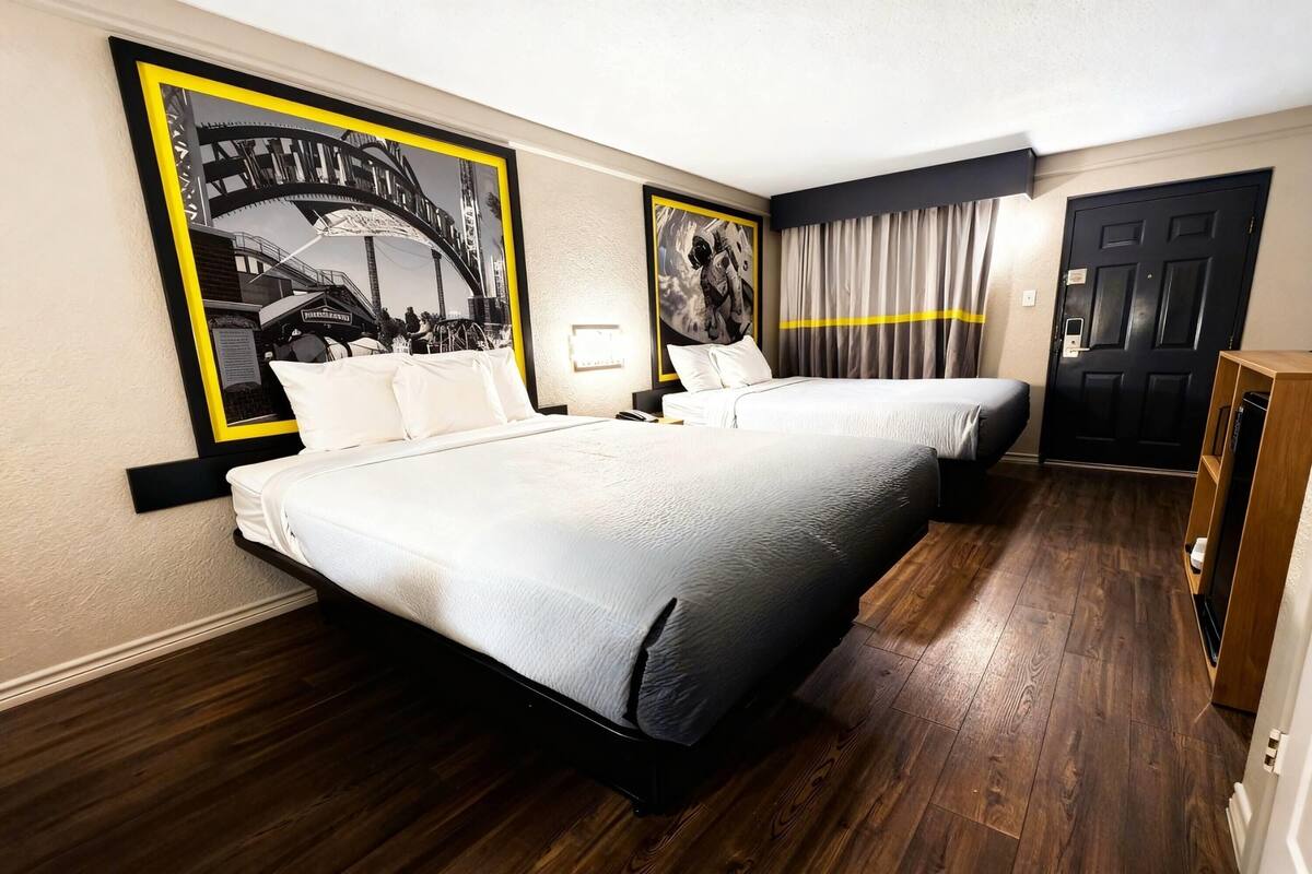A hotel room with two beds, wooden flooring, a black door, and a wall with framed pictures.