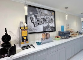 A modern kitchen with a large flat-screen TV displaying a welcome message, a waffle maker, and various food items on the counter.