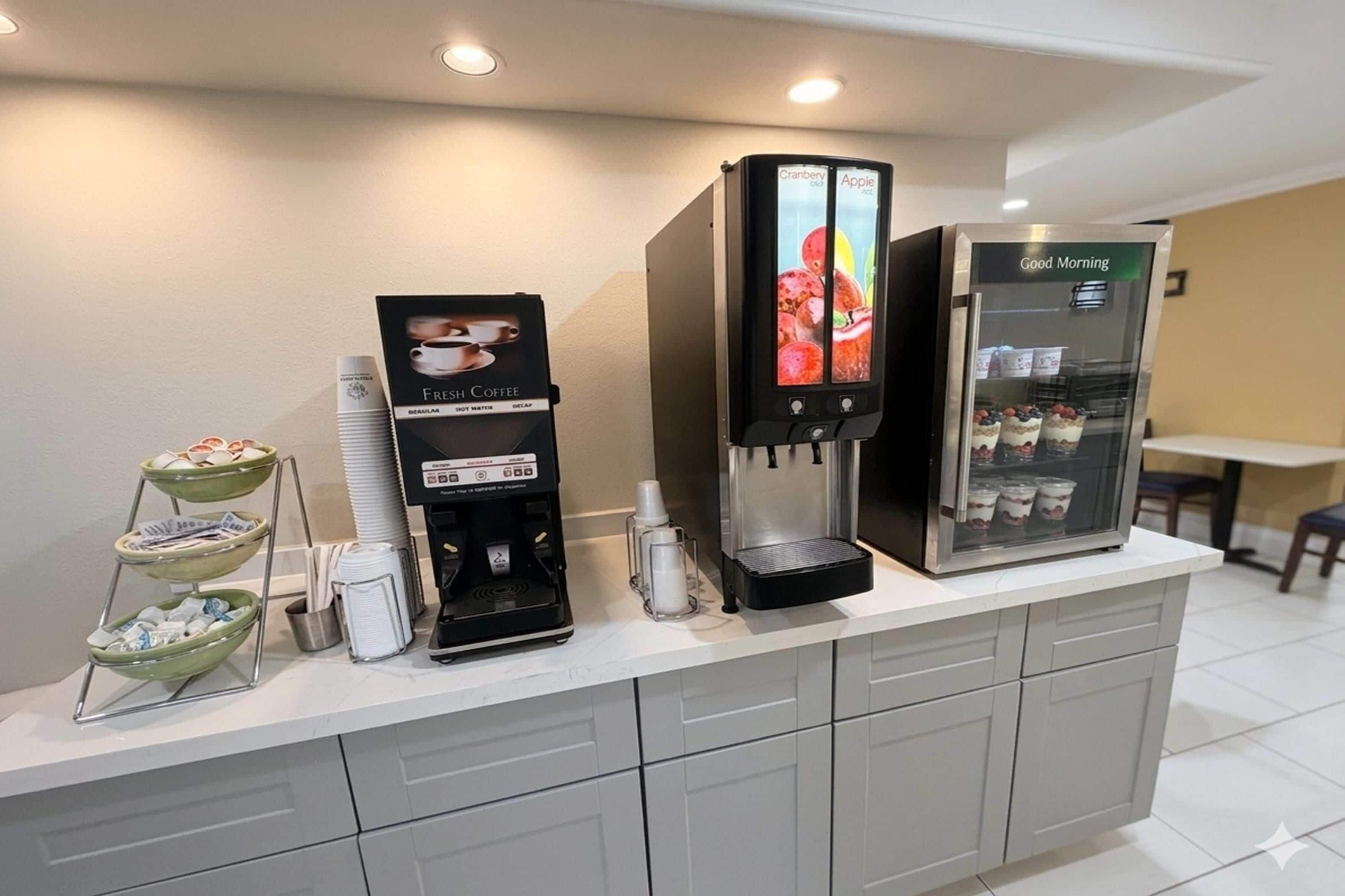 A coffee station with a coffee machine, a beverage dispenser, and a refrigerated display with drinks.