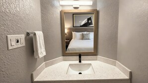 Une salle de bain avec un lavabo blanc, une serviette suspendue à un porte-serviettes, un miroir avec un cadre en bois et un luminaire fixé au mur.