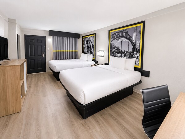 Habitación de hotel con dos camas, un escritorio, una silla, un televisor y una puerta.