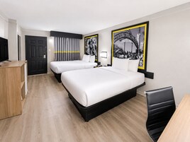 Habitación de hotel con dos camas, un escritorio, una silla, un televisor y una puerta.
