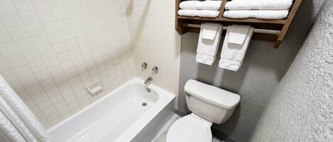 A bathroom with a bathtub, toilet, and a shelf with towels.