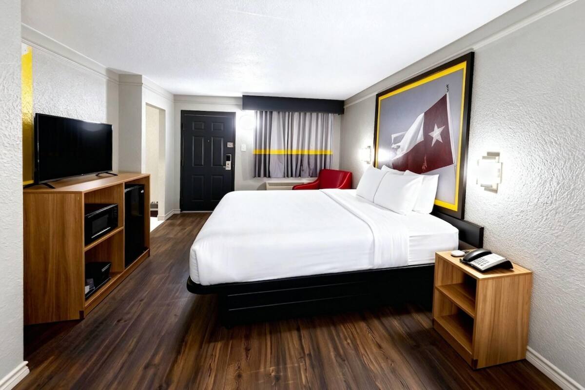 A hotel room with a bed, a TV, a desk with a phone, and a wall with a flag.