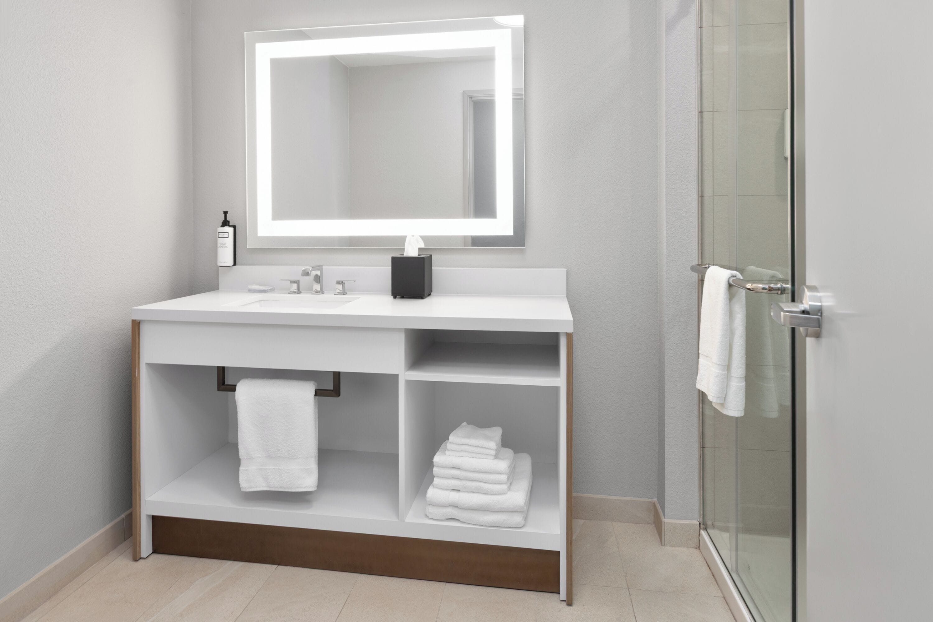 A modern bathroom with a white vanity, a large mirror, a glass shower enclosure, and a towel rack.