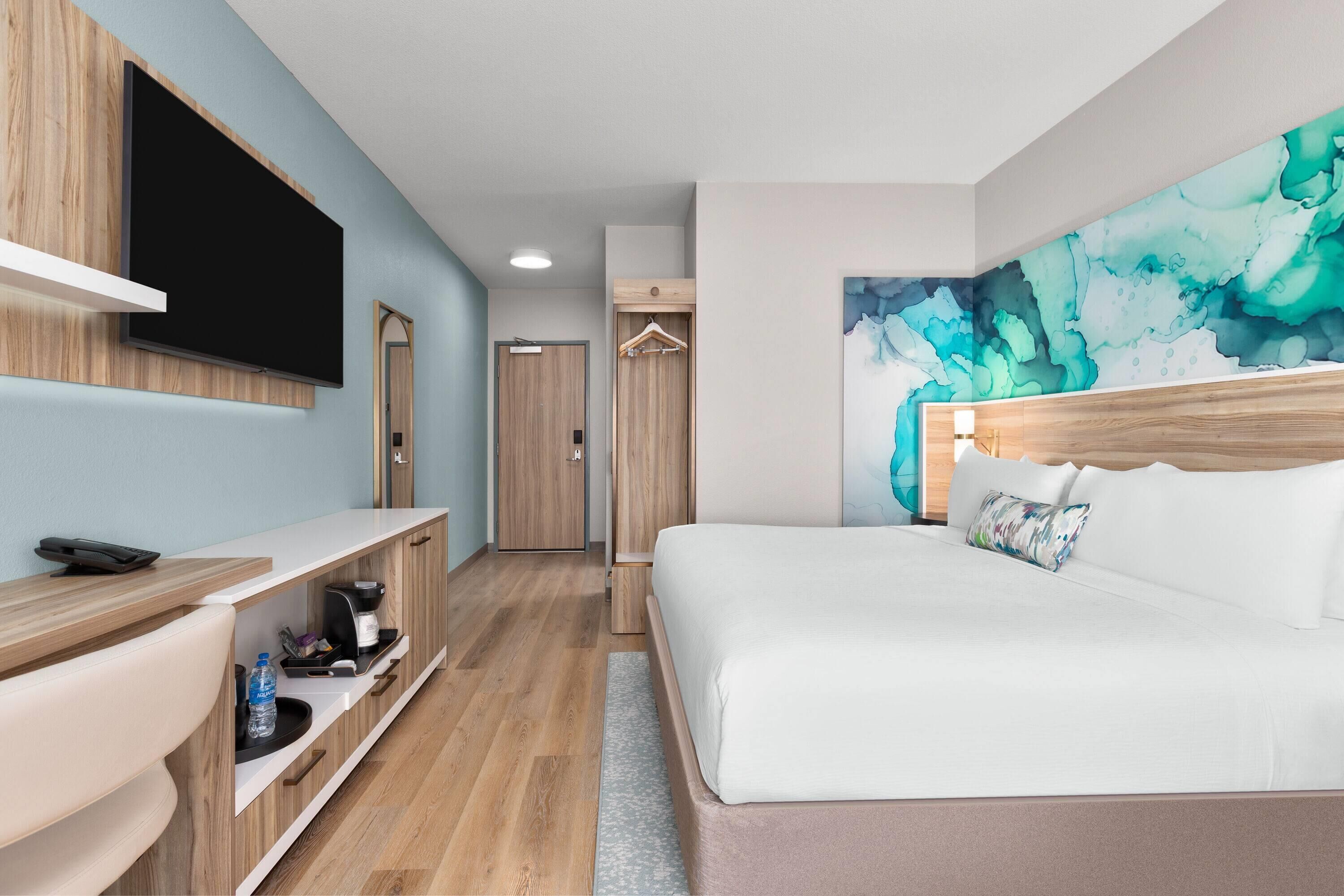 Habitación de hotel con cama, televisión montada en la pared, escritorio con teléfono y un cuadro en la pared.