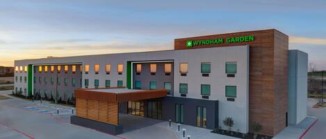 A modern hotel building with a sign reading 'WYNDHAM GARDEN.' It features a flat roof, multiple windows, and a covered entrance area.