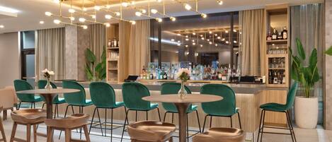 A bar area with green chairs and a bar counter stocked with bottles.