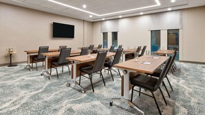 A conference room with multiple tables and chairs, a flat-screen TV mounted on the wall, and a carpeted floor. - Wyndham Garden Anna (Anna)