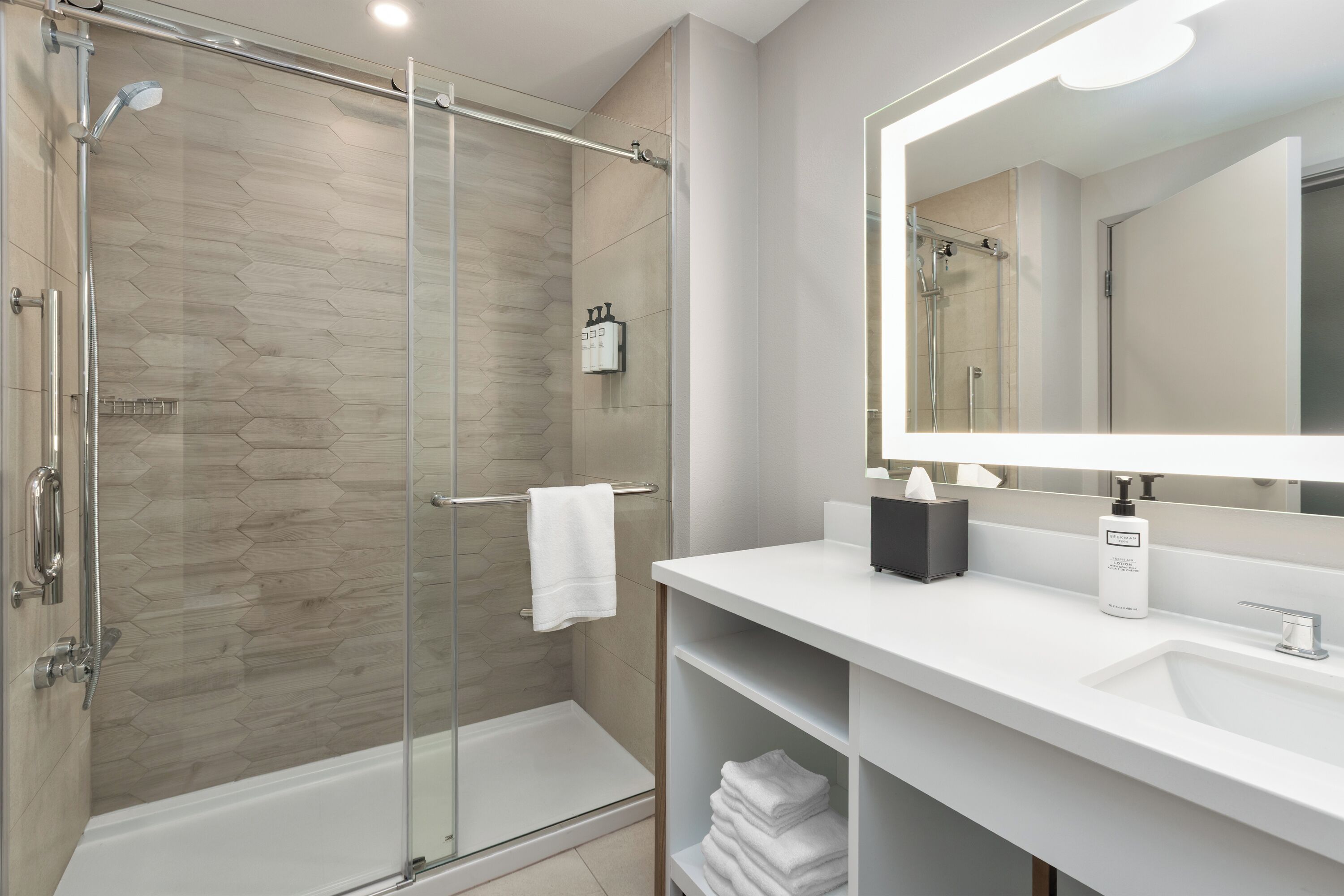 A modern bathroom with a glass-enclosed shower, a white sink, and a large mirror.