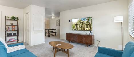Sala de estar moderna com sofás azuis, mesa de centro de madeira, pintura de cacto grande e decoração minimalista.
