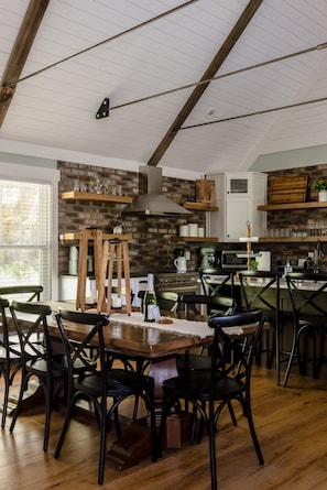 A modern kitchen with a brick wall, wooden shelves, and a dining area with a wooden table and chairs.