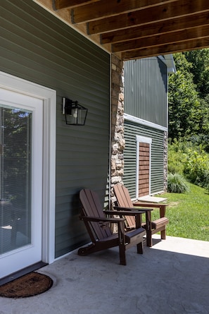 A covered patio area with Adirondack chairs and a table, a stone pillar, and a house with green siding and a stone facade.