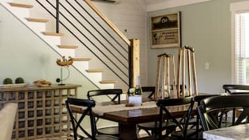 Un coin repas avec une table en bois, des chaises noires, un meuble à vin et un escalier avec un plafond blanc.