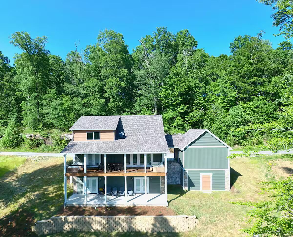 Une maison à deux étages avec un balcon, un garage et un jardin arboré à l’arrière.