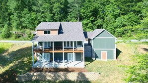 A two-story house with a balcony, a garage, and a wooded backdrop.