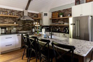 A modern kitchen with a central island, bar stools, a stainless steel refrigerator, and a brick wall backsplash.