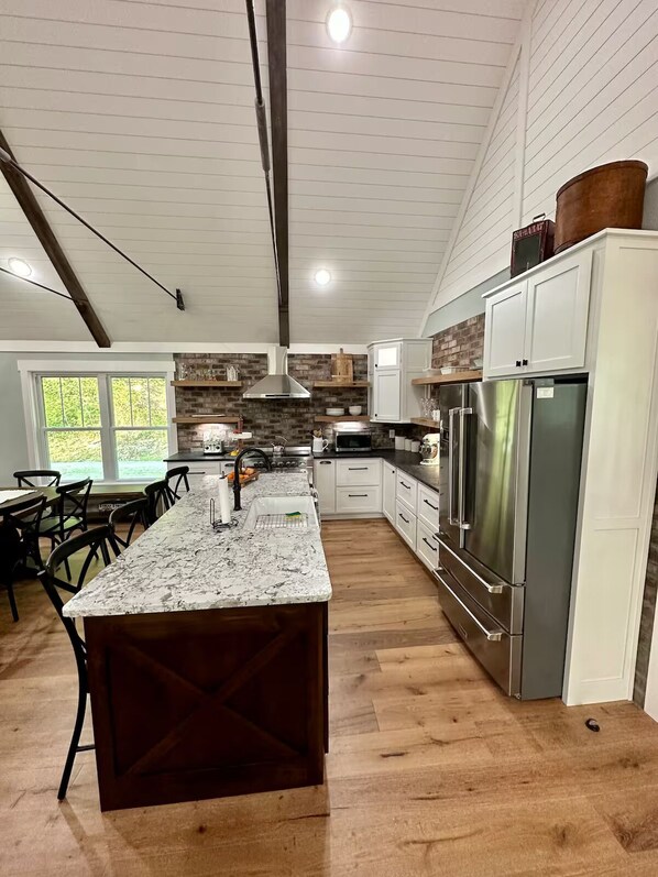A modern kitchen with a large island, stainless steel appliances, and a brick accent wall. - Rough River Lake - 5BR Waterfront Home - Sleeps 15 - Firepit (Westview)