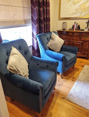 Two blue armchairs with cushions, a wooden cabinet, and a rug on a wooden floor.