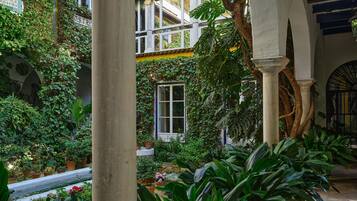 A lush courtyard with a variety of plants, a window with a view, and a traditional architectural style with columns and arches.