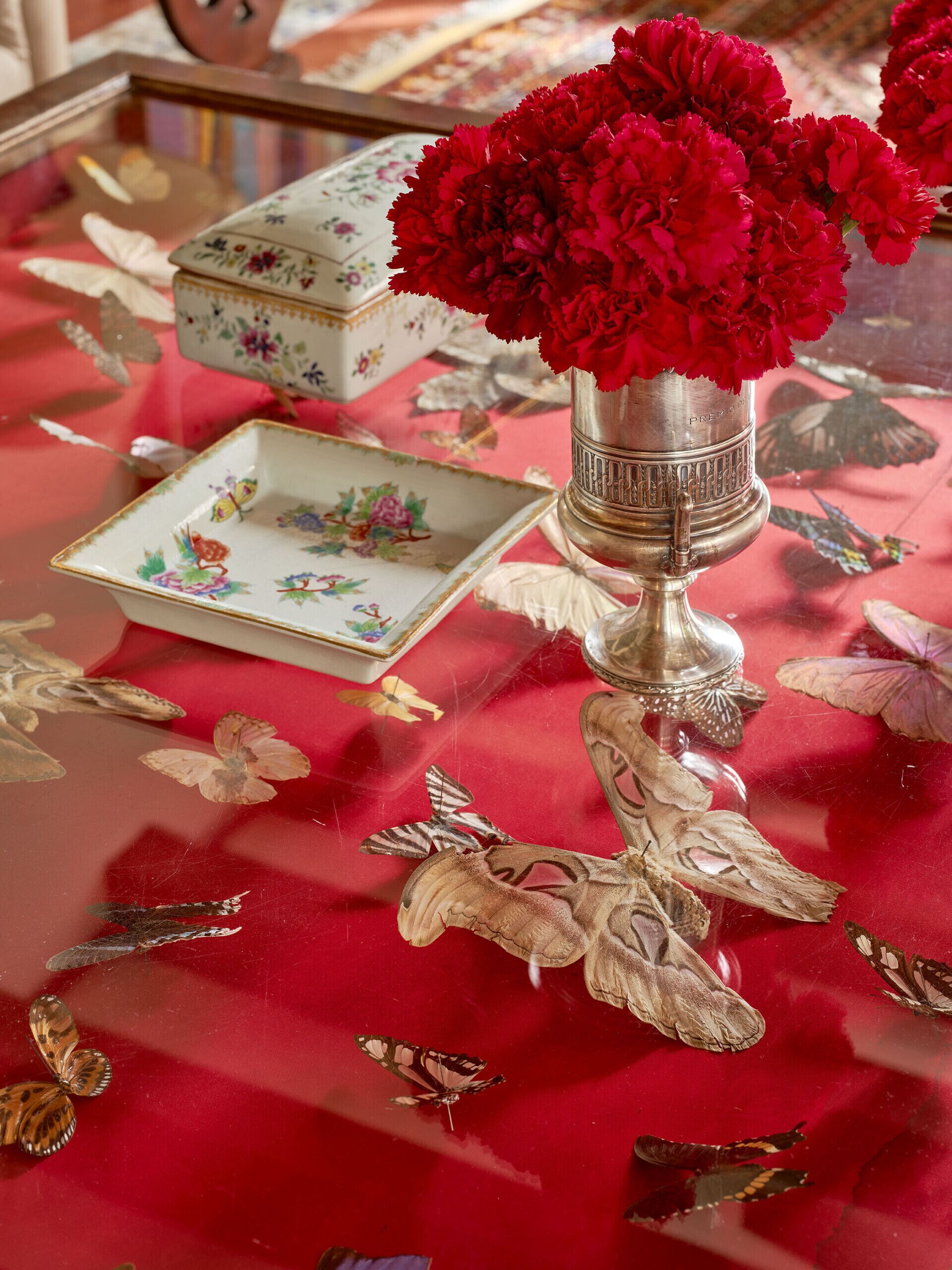 Ein Tisch mit roter Tischdecke, einer silbernen Vase mit roten Blumen, einem Dekorationsplatten und Schmetterlingsdekorationen.