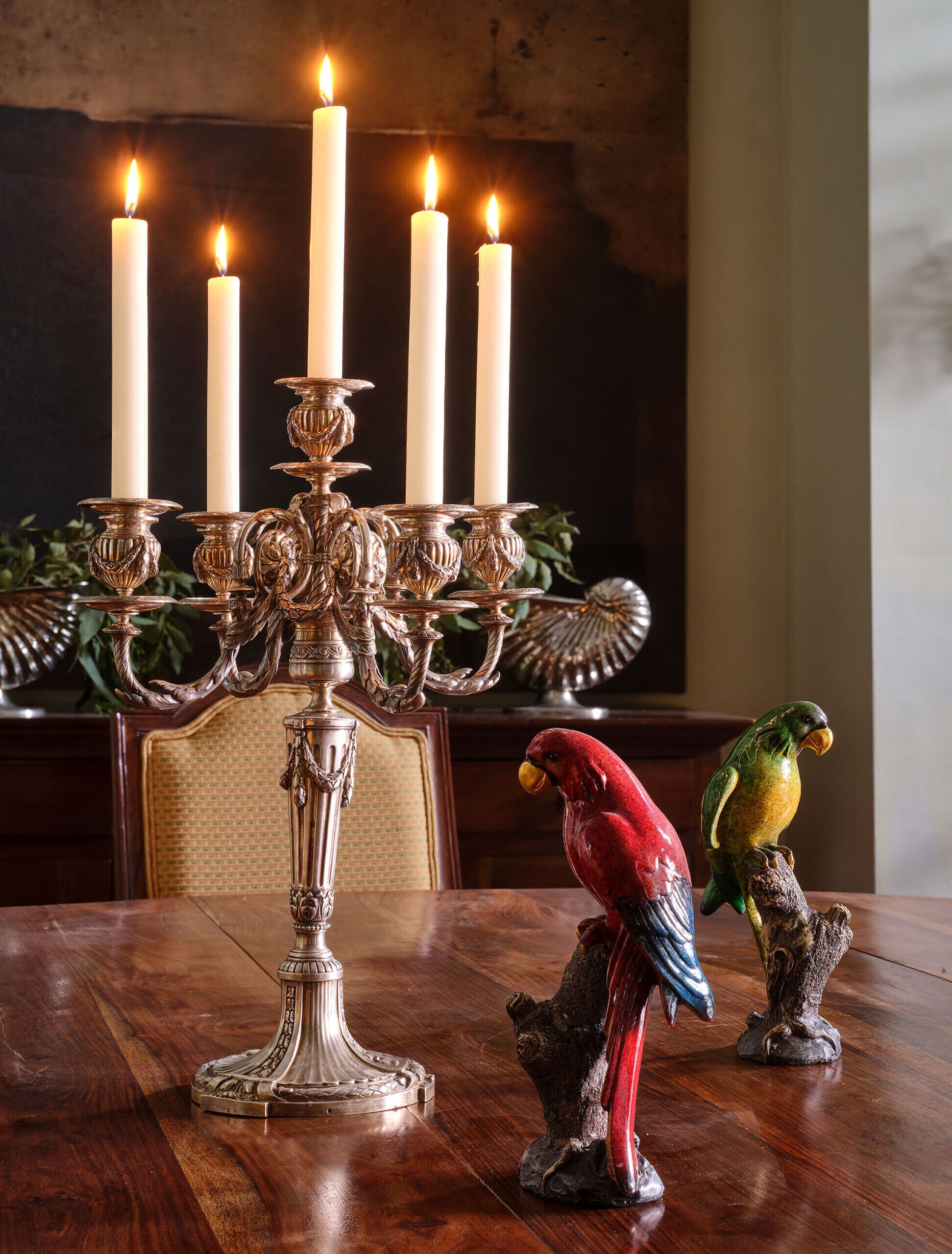Een eettafel met een kandelaar met zes brandende kaarsen, een decoratief papegaai beeldje en een rustieke vogelsculptuur.