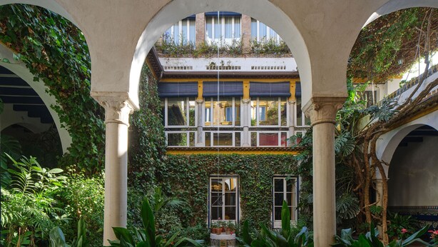 An indoor courtyard with arches, potted plants, a central pool, and a building with windows and balconies.