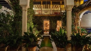 A courtyard with arches, potted plants, a small pool, and a balcony with a view of the night sky.