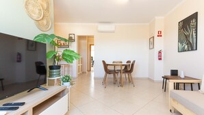A modern living room with a flat-screen TV, a dining area with a table and chairs, and a small sofa. - Azura Apartment with 2 Bedrooms (Conceição de Tavira)