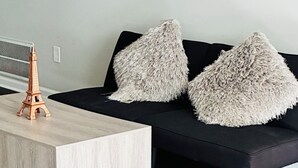 A modern living room with a wooden coffee table, a black sofa with fluffy pillows, and a colorful rug.