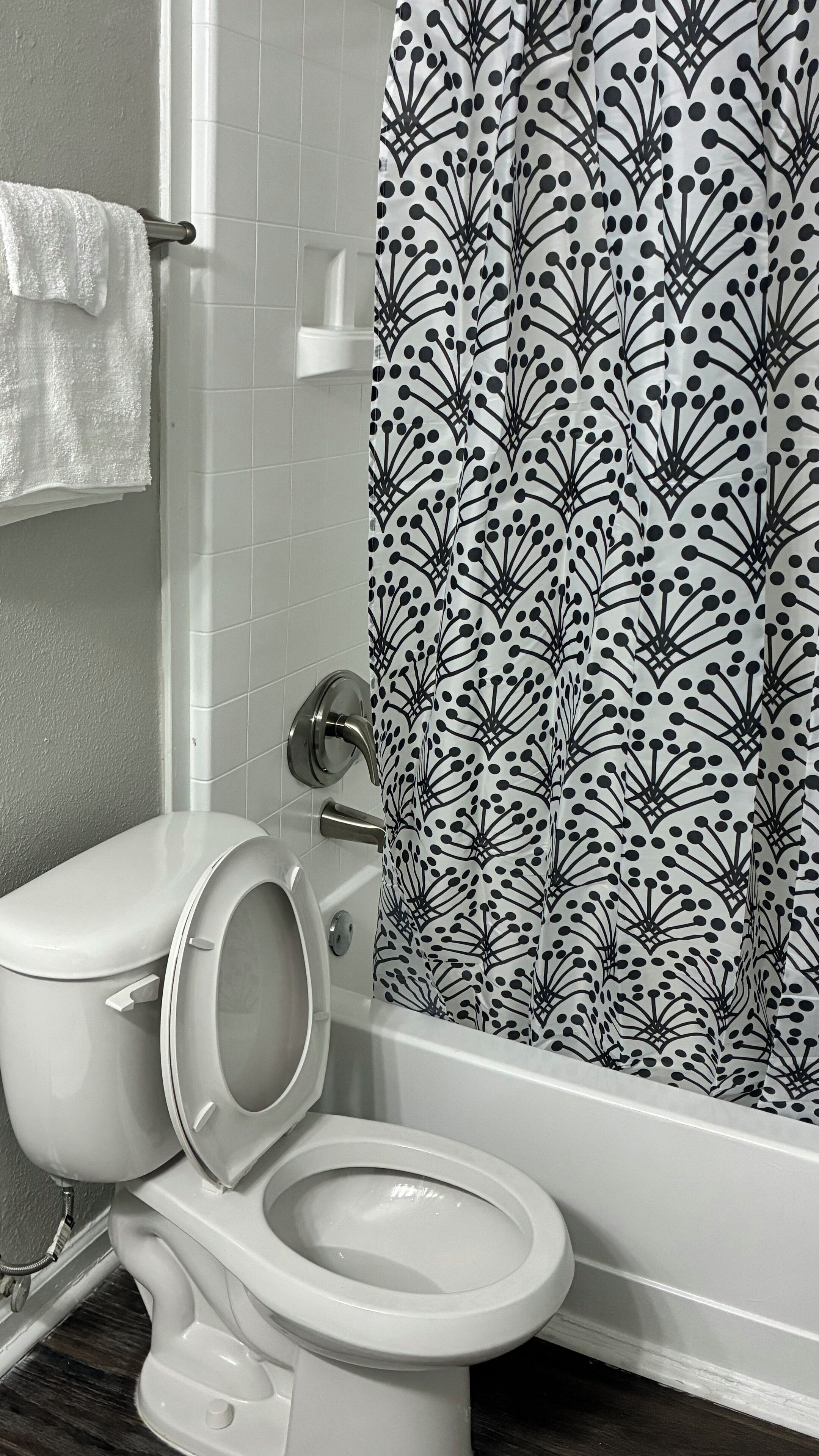A bathroom with a toilet, a towel rack, and a shower curtain with a black and white pattern.