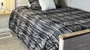 A bedroom with a wooden headboard, a black and white striped bedspread, and a single white pillow.