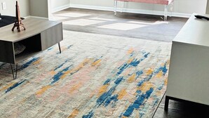 A spacious room with a large, colorful rug, a bench, and a desk.