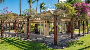 Un espacio exterior cubierto con puerta de cristal, rodeado de palmeras y plantas con flores.