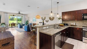 Una cocina moderna con encimeras de granito, armarios de madera oscura y un horno empotrado. Hay una zona de comedor con mesa y sillas, y un amplio ventanal con vistas al exterior.