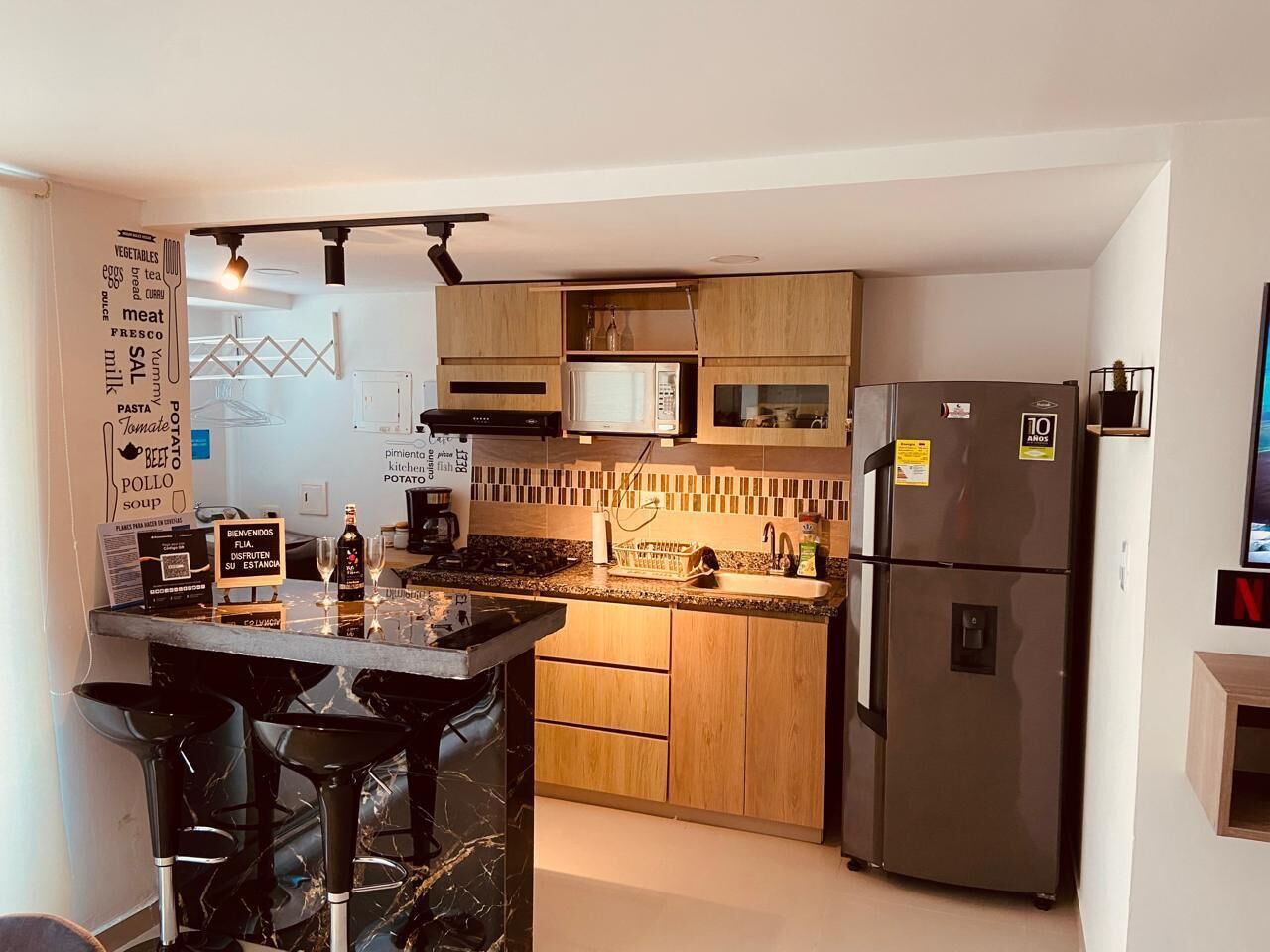 Une cuisine compacte dotée d’un îlot central, de meubles en bois, d’un réfrigérateur et d’un four à micro-ondes.