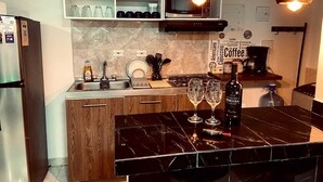 A modern kitchen with a marble countertop, wooden cabinets, a built-in microwave, and a coffee station.