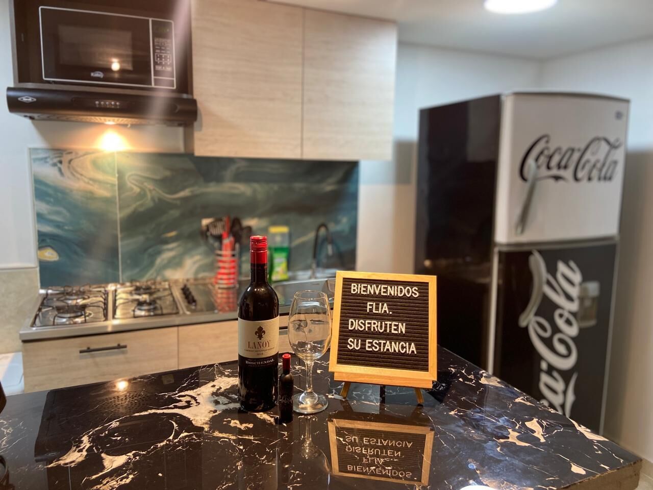 A kitchen counter with a bottle of wine, a glass, and a welcome sign.