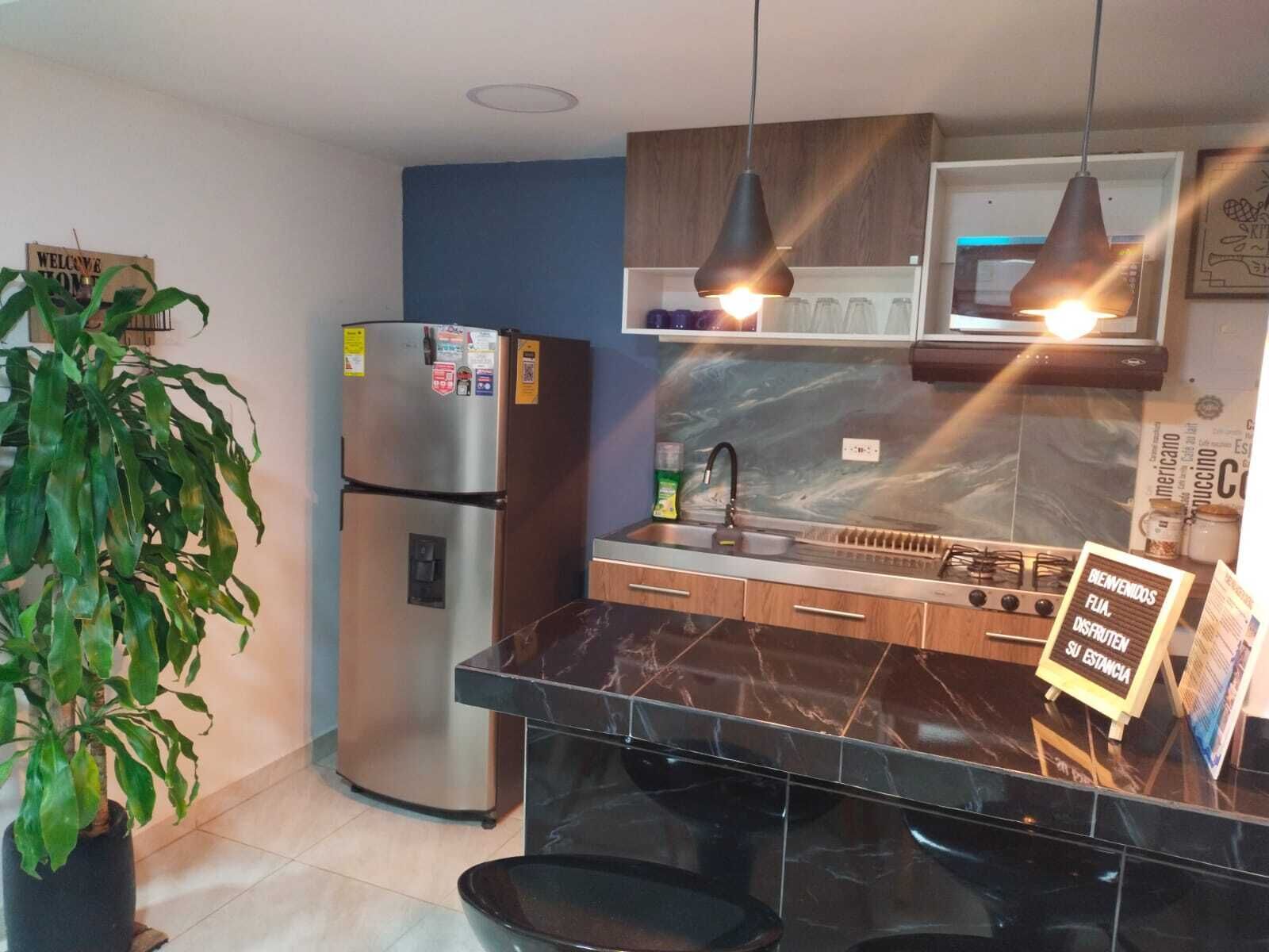 Una cocina moderna con encimera de mármol negro, electrodomésticos de acero inoxidable, armarios de madera e iluminación colgante.