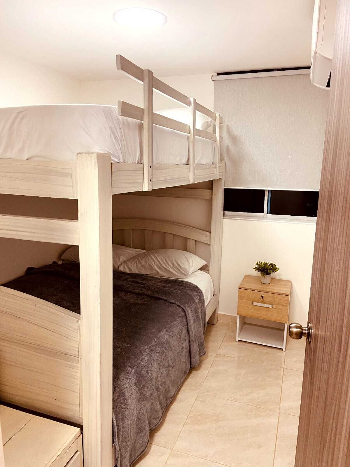 A bunk bed room with a small bedside table and a window with curtains.