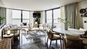 A spacious living room with a large window, a flat-screen TV, and a dining area with a round table and chairs. - 🌿 Jungle Penthouse w/ Private Pool | 4 Min to Beach + Town (Tulum)