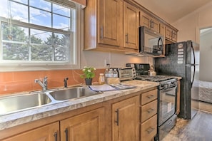 A kitchen with wooden cabinets, a stainless steel sink, a microwave, a stove, and a refrigerator. - Fresh Air Pocono Escape | Suites & Cottages (Pleasant Mount)