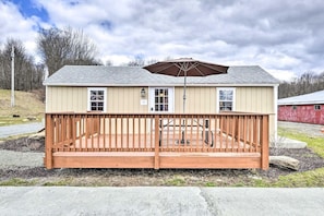A single-story building with a wooden deck, a covered patio area, and a red barn in the background. - Fresh Air Pocono Escape | Suites & Cottages (Pleasant Mount)